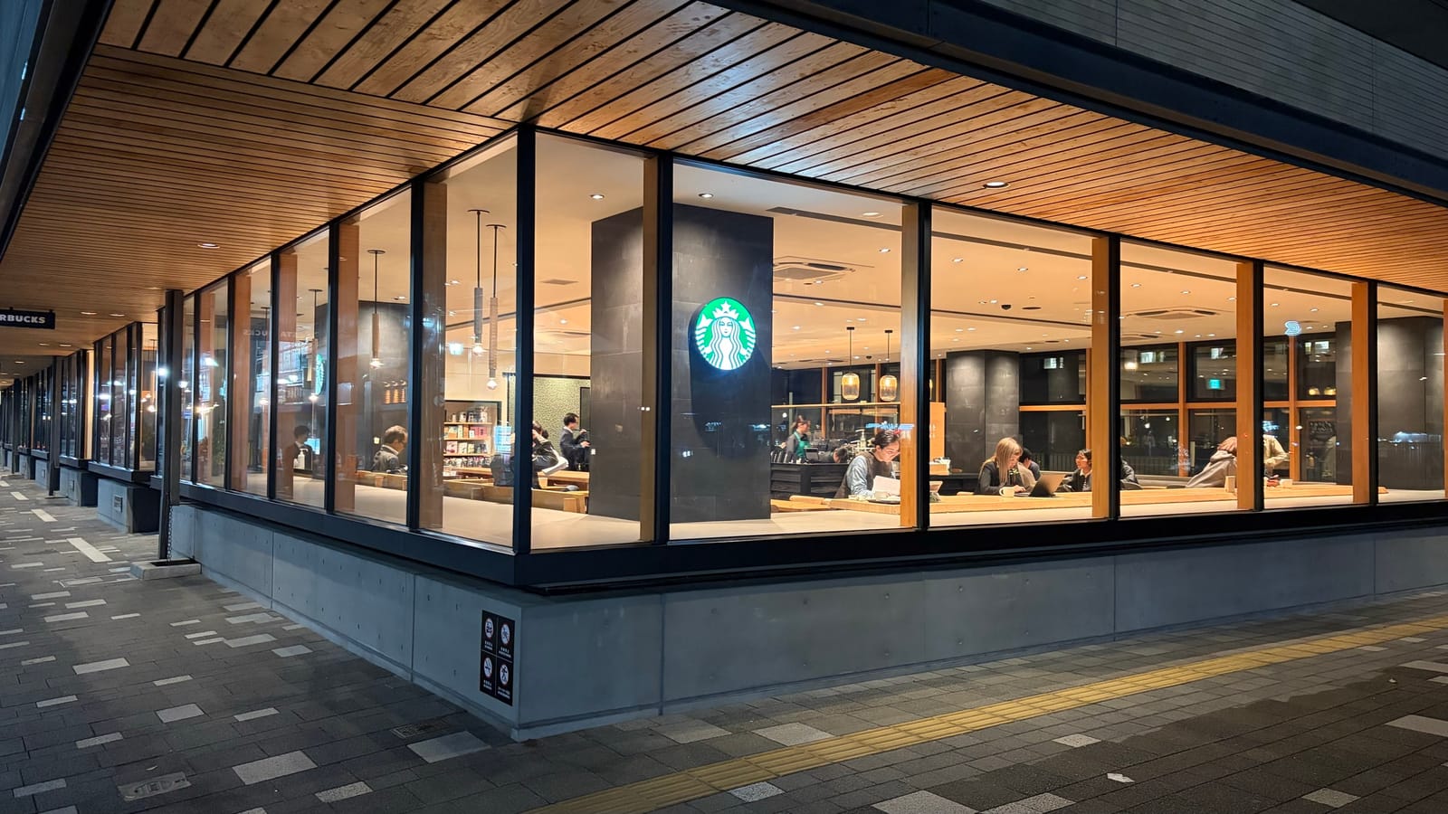 夜の京都市役所店の外観。コーナーいっぱいに広がるガラス張りと木の天井、中央のサイレンロゴが暖色の店内に浮かぶ