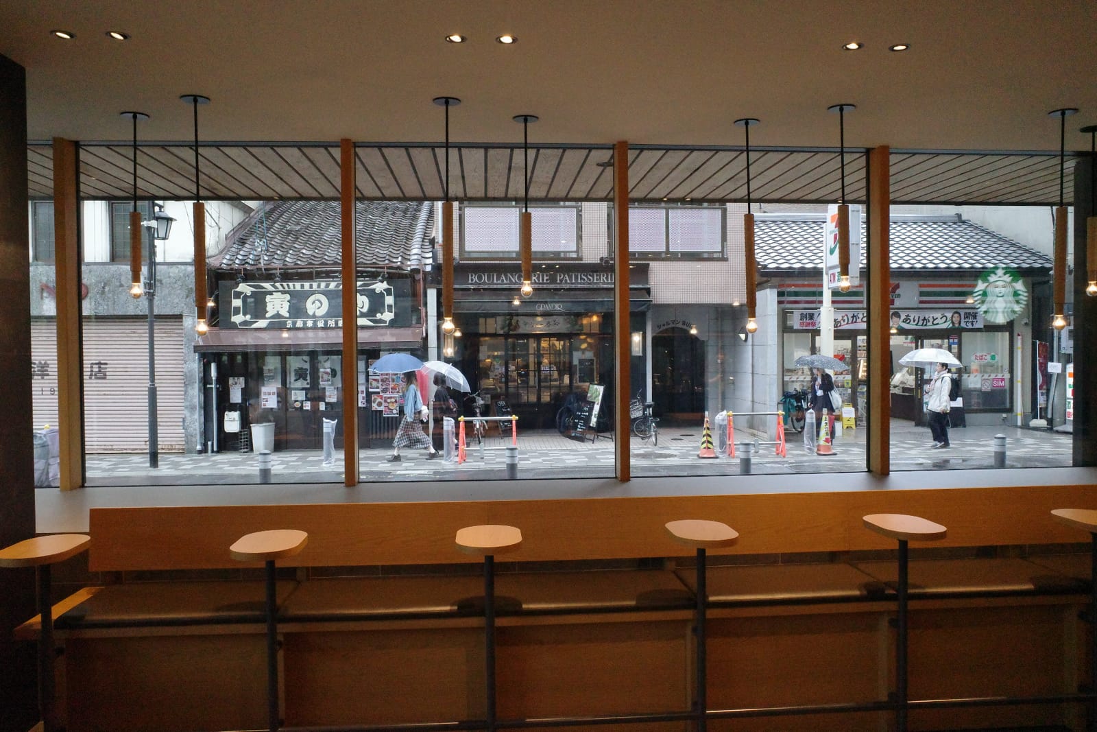 寺町通商店街側のカウンター席。木のスツールが並び、窓の外には商店街の小さな店並みと傘をさす人々