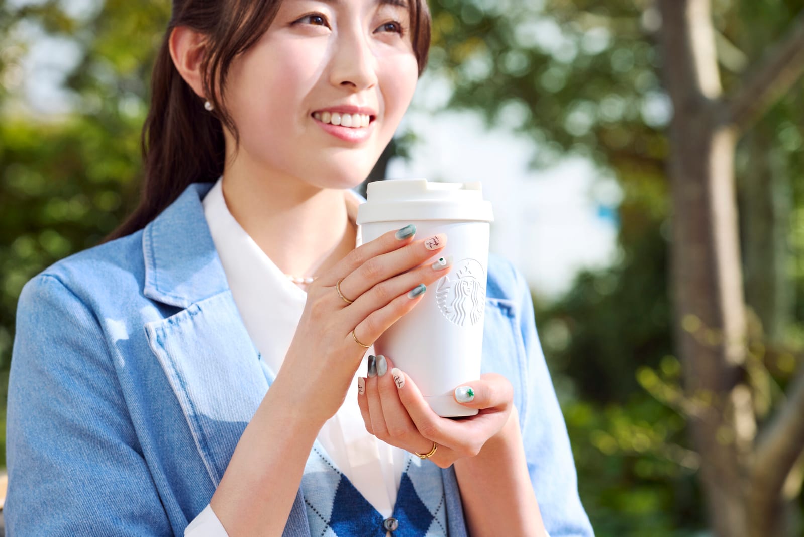 スターバックスグリーンのネイルを着けた手で、白いリユーザブルカップを持つ様子