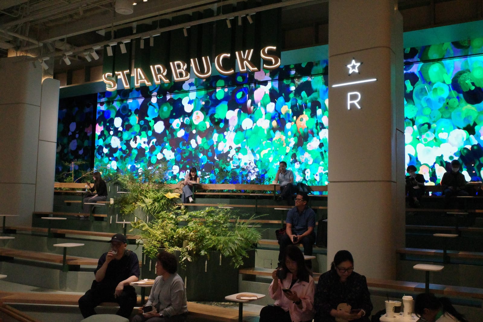 段差のテラス席と、印象派風の壁面ミューラル。STARBUCKS のロゴと Reserve の R マークが浮かぶ